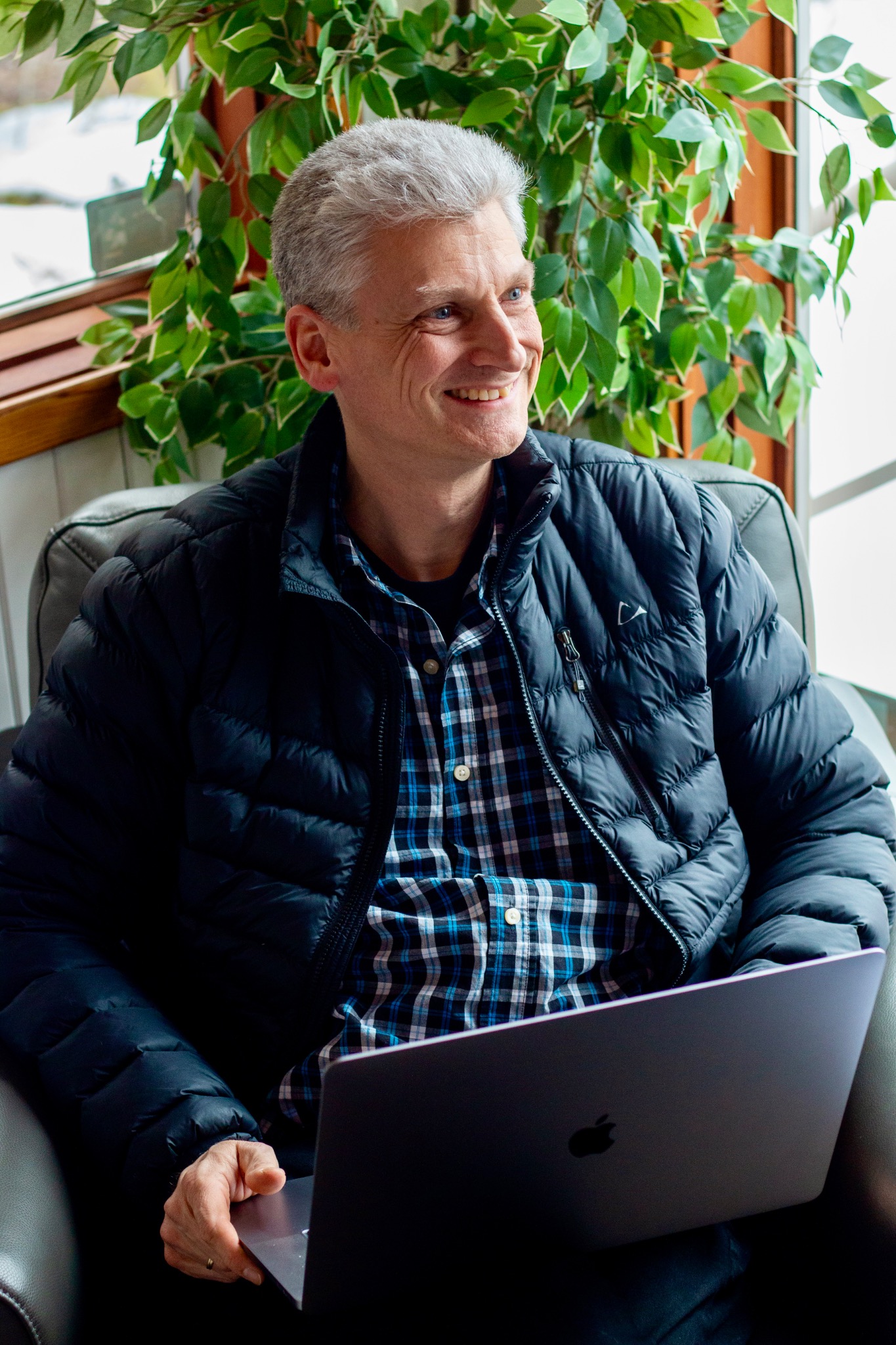 Marc smiling with a laptop in a bright, plant-filled space
